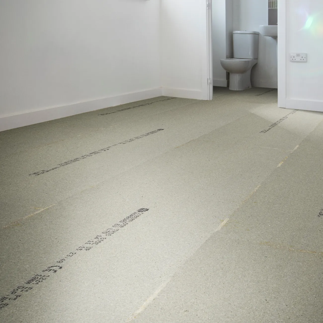 Empty room with a light gray underlayment floor, white walls, and a view into a bathroom with a toilet.